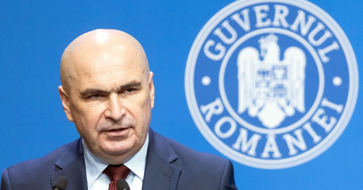 Ilie Bolojan vorbește în timp ce pe fundal se vede sigla Guvernului României, iunie 2025