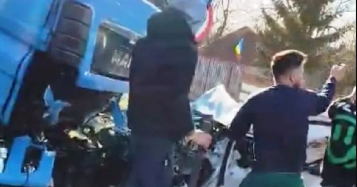 Accident rutier între o mașină albă și un TIR, mașina a fost complet distrusă, iar martorii încearcă să salveze pasagerii