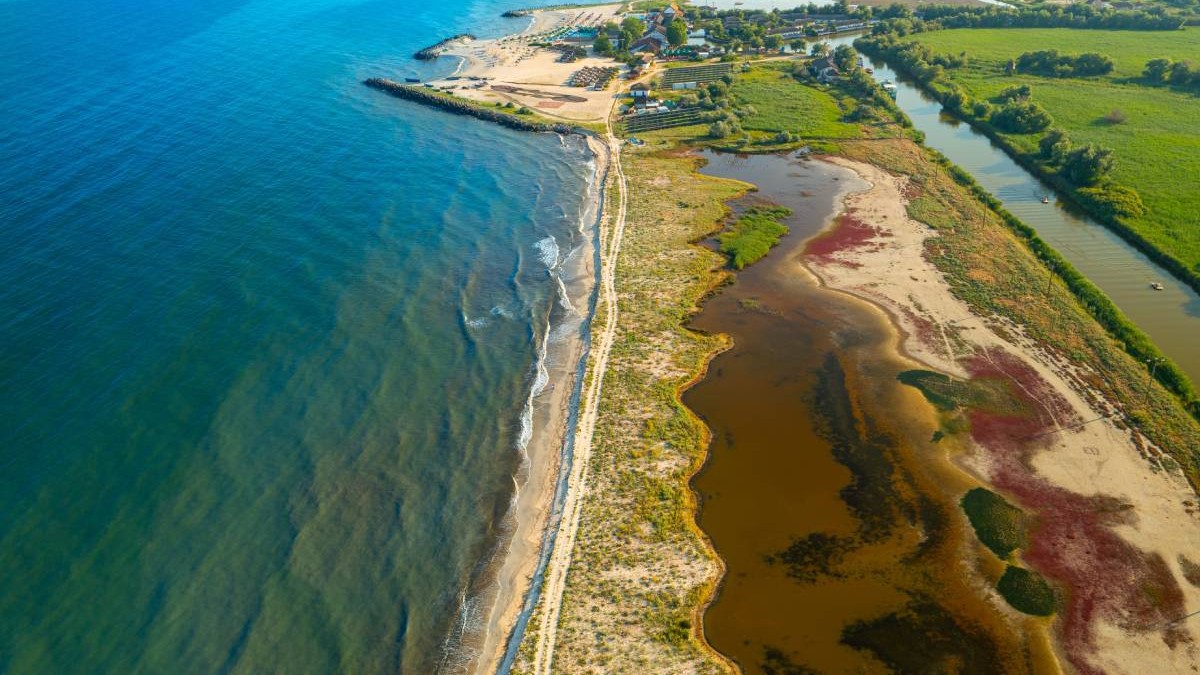 Țărmul Mării Negre în Delta Dunării. Vedere aeriană asupra acestei uimitoare Gure Portiței din România, într-o frumoasă zi însorită. Peisaj cu apă albastră de mare și alge roșii.
