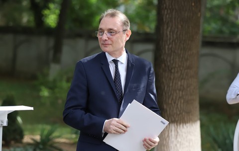 Luca Niculescu, îmbrăcat într-un sacou negru, o cămașă albă și o cravată neagră cu buline albe, ținând mâinile apropiate de corp și în fața trunchiului, cu o foaie de hârtie în mână