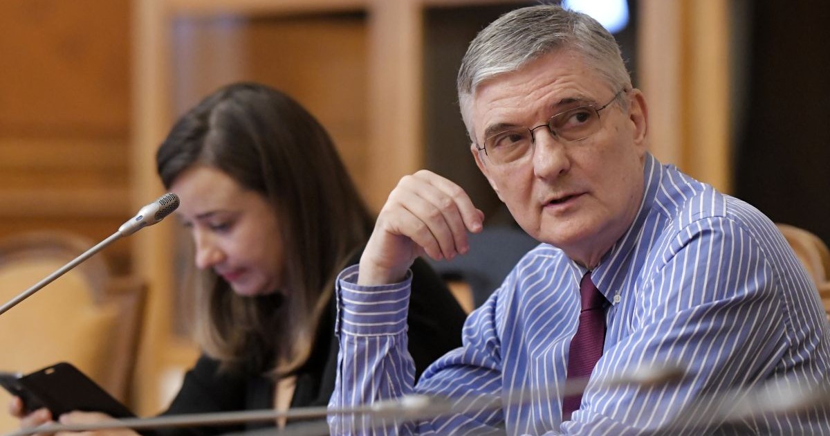 Daniel Dăianu, președintele Consiliului Fiscal, într-o cămașă cu dungi albe și albastre la o conferință, în fața unui microfon