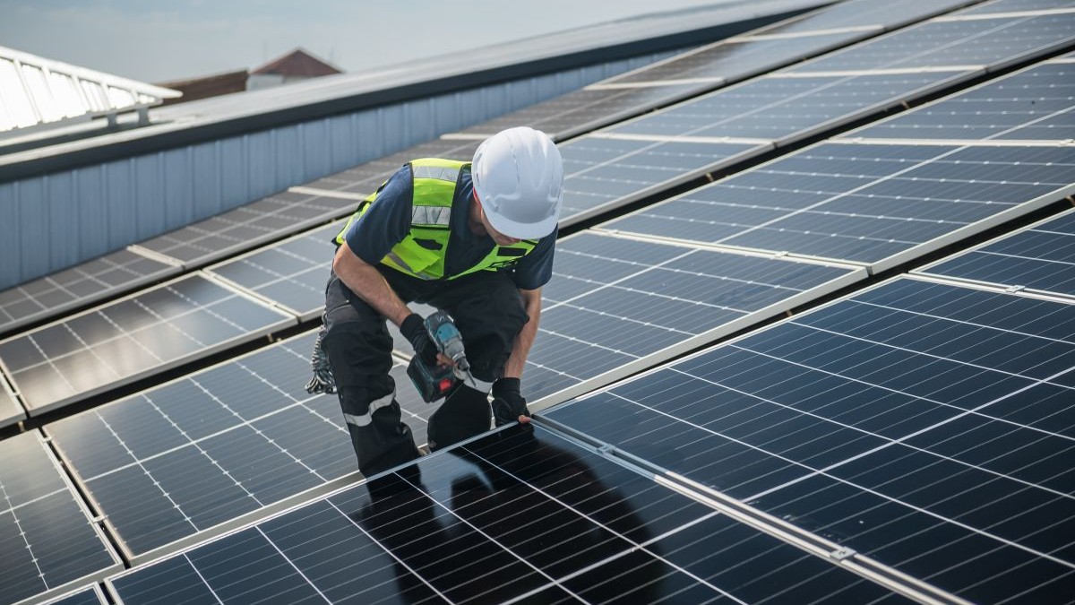 Un tehnician instalează panouri solare pe acoperișul unei fabrici pentru energie verde