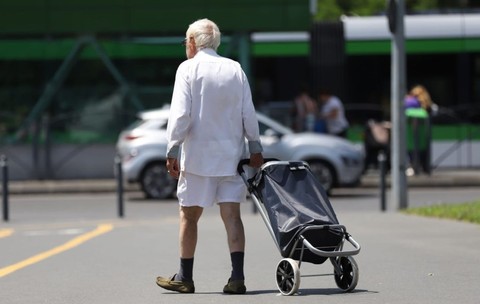 Un pensionar îmbrăcat în alb, fotografiat cu spatele, merge pe stradă cu un căruț de piață, în București, iulie 2026. Foto: Libertatea/ Dumitru Angelescu