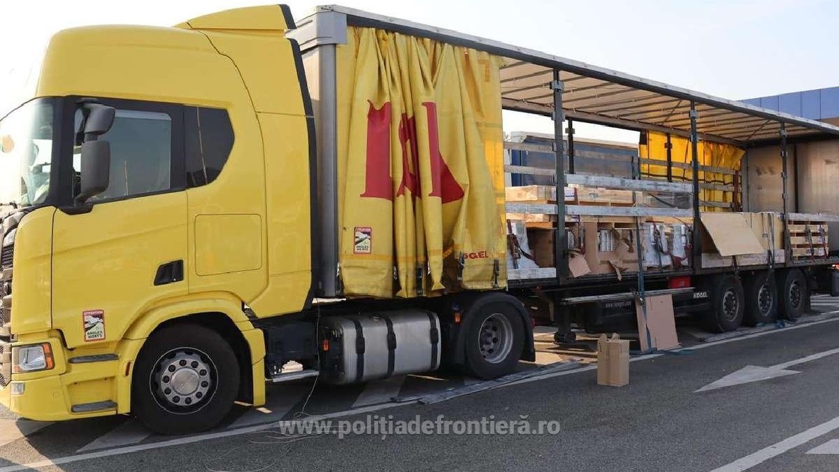 Un camion galben cu prelata de la remorca data la o parte, se vad mai multe cutii si paleti in remorca