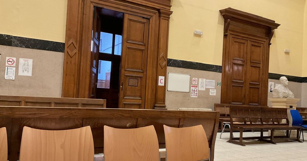 Fotografie a holului unui tribunal cu uși duble din lemn, pereți bej și un rând de scaune goale în prim-plan