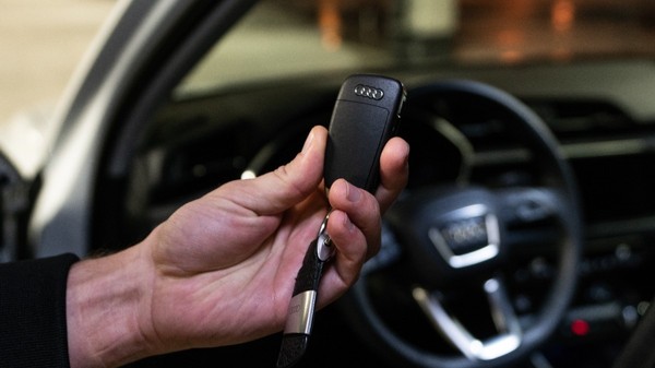 Un bărbat care ține cheile unui AUDI, care se vede în fundal