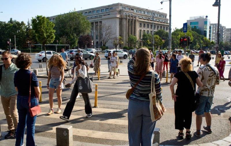 București, România – 25 iunie 2024: Oamenii traversează strada în apropierea Palatului Victoria, care găzduiește sediul Guvernului României, în București.