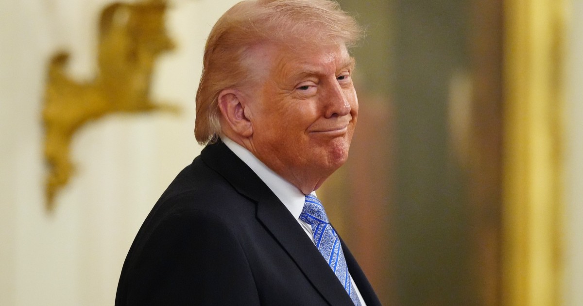 Donald Trump din profil, îmbrăcat în costum negru, cămașă albă și o cravată albastră, schițând un zâmbet