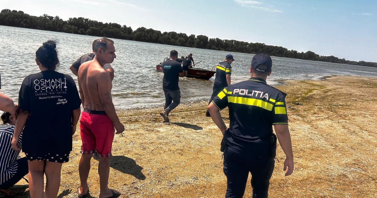 doi ofițeri de poliție, îmbrăcați în uniforme negre cu înscrisuri verzi fosforescent, alături de alți martori. stau în apropierea unei bărbați poziționate pe o plajă neamenajată din zona Gostinu, județul Giurgiu