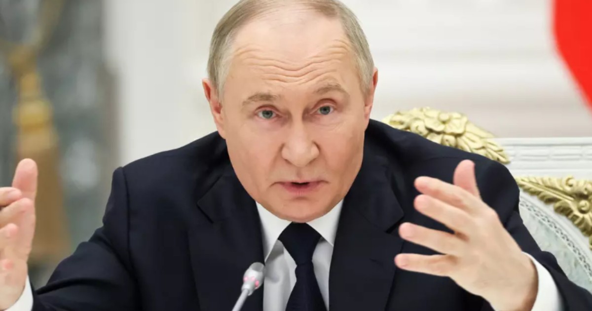 În imagine este ilustrat Vladimir Putin, în costum negru și cămașă albă. Acesta susține un interviu