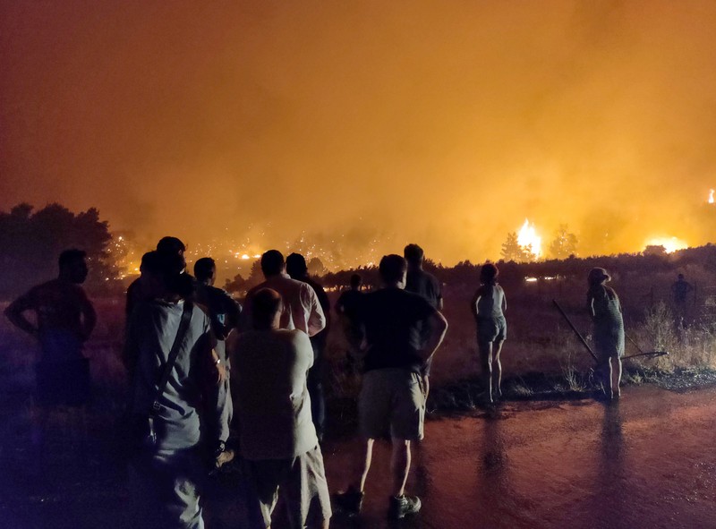 Locuitorii insulei Evia urmăresc un incendiu de vegetație din zona Limni. | Foto: EPA