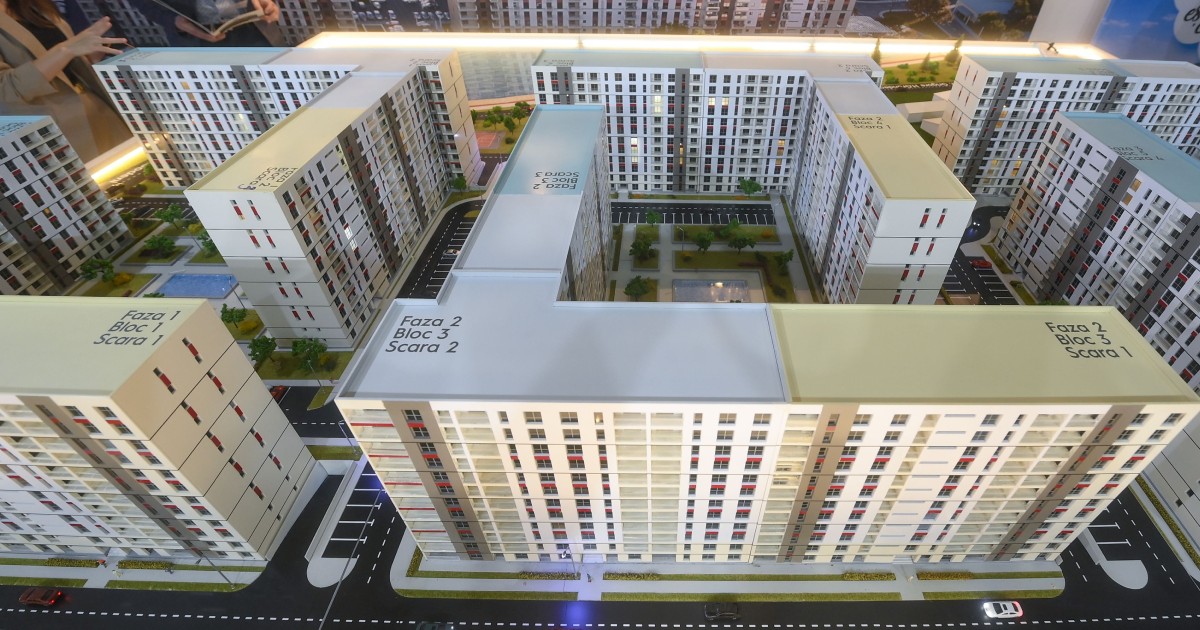 Imaginea arată o machetă arhitecturală a unui ansamblu rezidențial format din mai multe blocuri de apartamente. Blocurile sunt dispuse în jurul unor curți interioare cu spații verzi și locuri de parcare