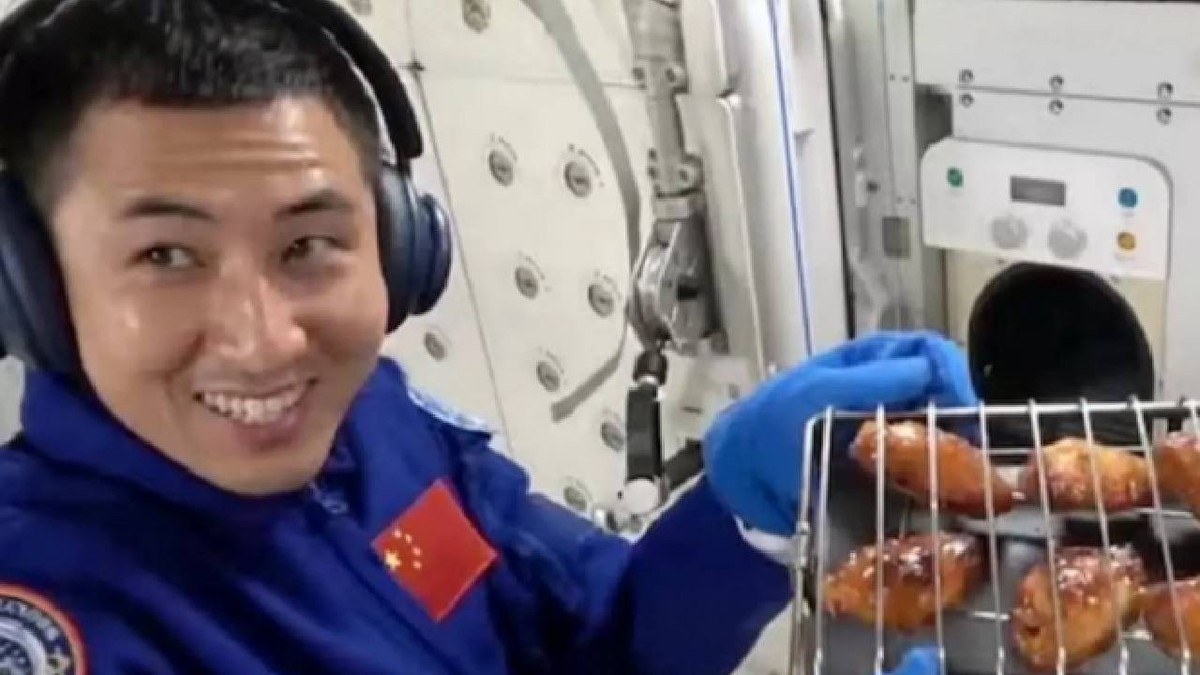 Un astronaut chinez ține în mâini un grătar pe care sunt așezate mai multe aripioare de pui proaspăt gătite