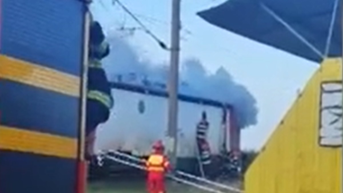 Un fum gros se ridică deasupra unei locomotive staționate în gara Plopeni, în timp ce trei pompieri intervin pentru tingerea incendiului, 3 august 2025