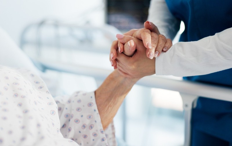 O persoană care ține mâna unei femei aflate pe un pat de spital