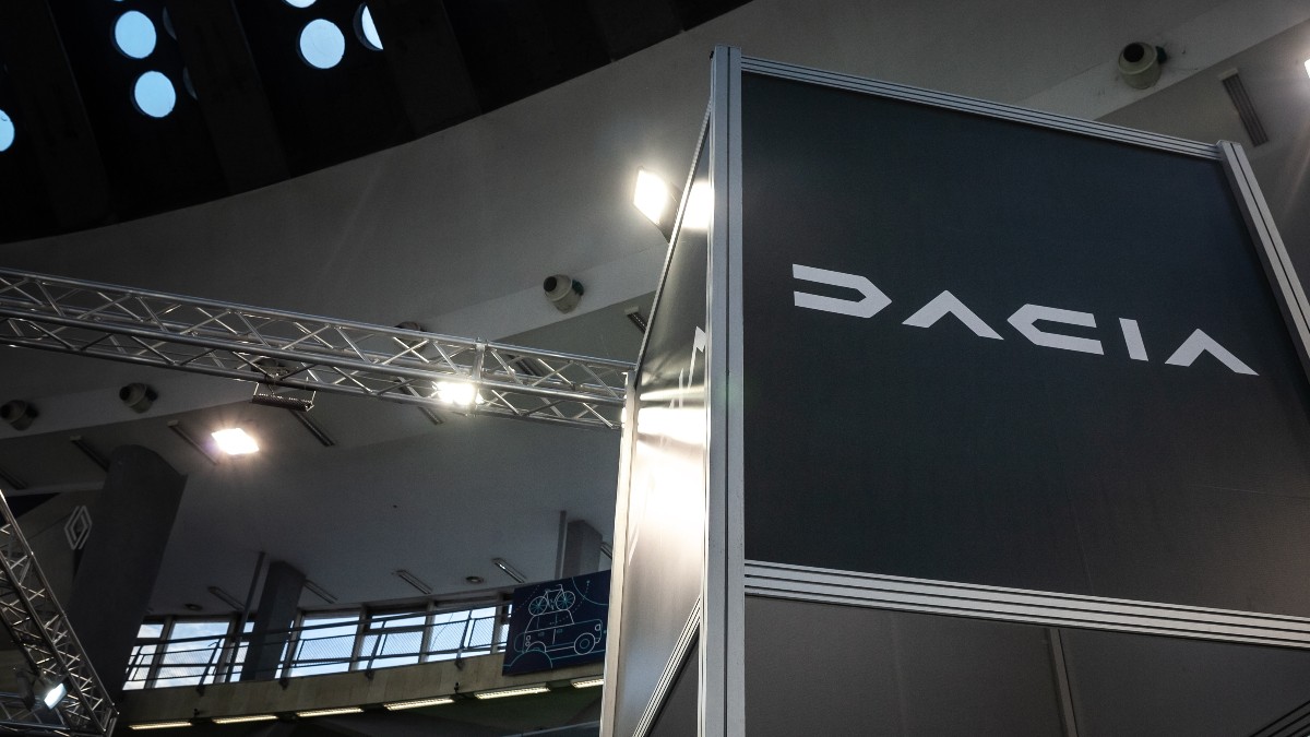 Logo-ul Dacia pe un stand de mari dimensiuni la un eveniment sau o expoziție, în interiorul unei clădiri moderne.