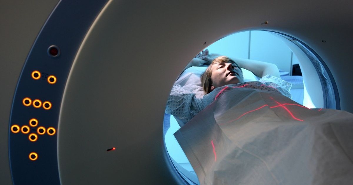 persoană în halat medical întinsă într-un aparat cu radiatii care efectuează o scanare CT