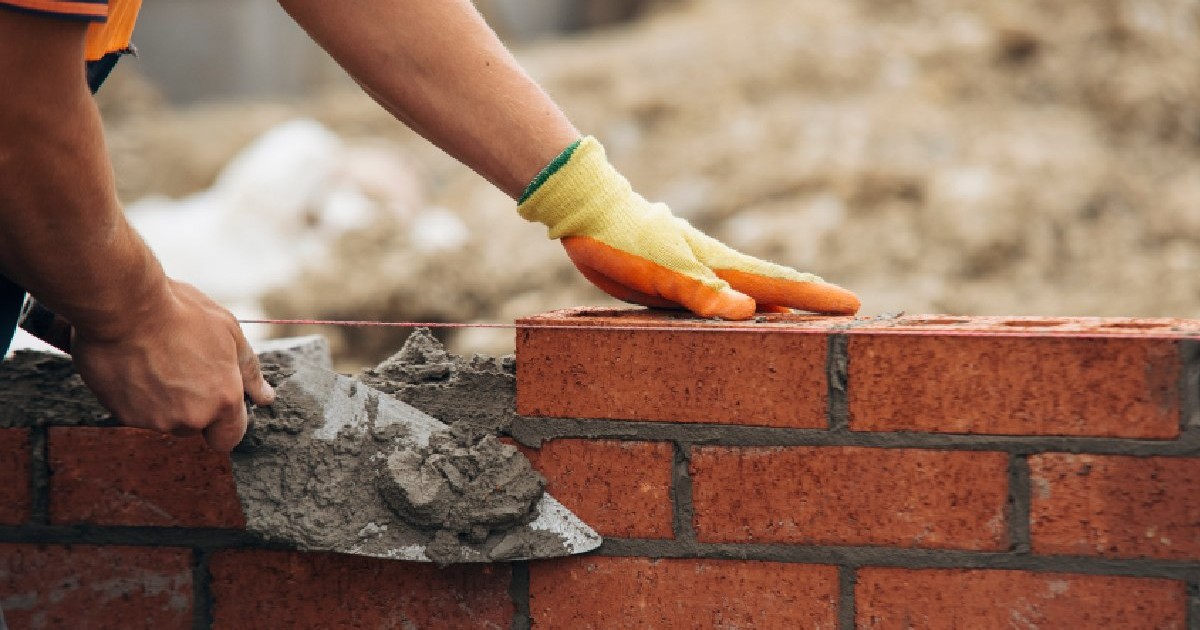 Muncitor în construcții care așează cărămizi roșii cu mistria și mortar