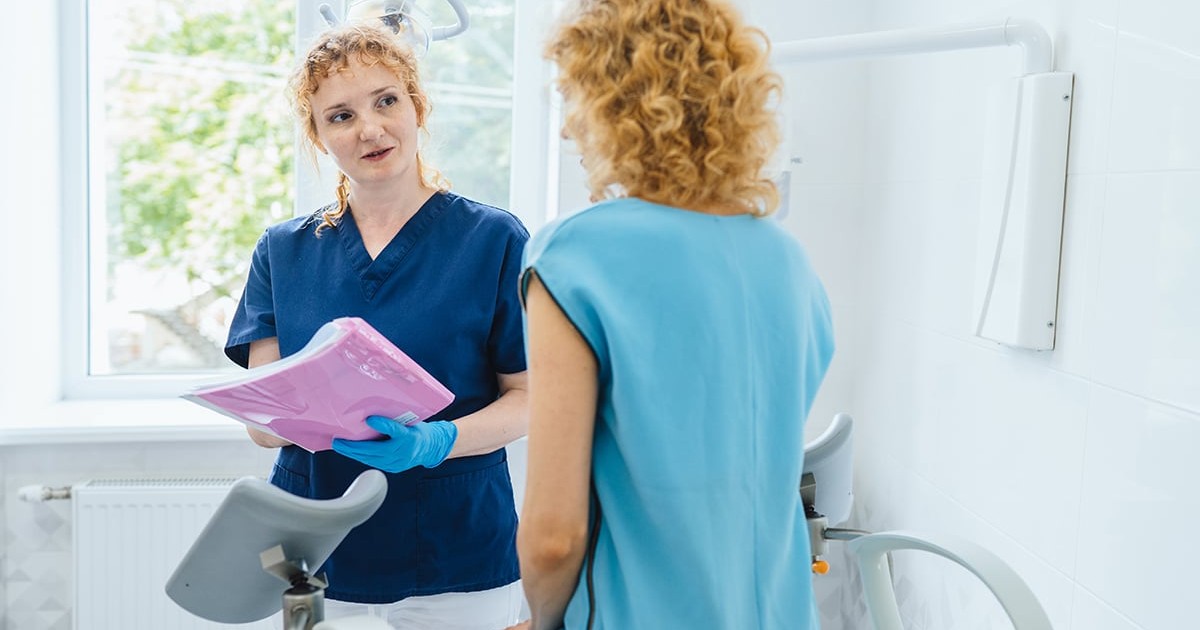 Ginecolog prietenos care lucrează cu o pacientă în clinică. Femeie blondă de vârstă mijlocie care are o consultație ginecologică stând pe un scaun într-o clinică medicală