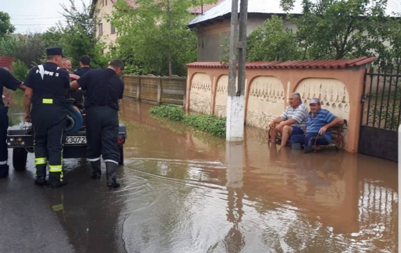 Doi bărbați din Țigănești, Teleorman, stau pe bancă și se uită la pompieri cum scot apa de pe ulițe. Imaginea e „virală” pe Internet