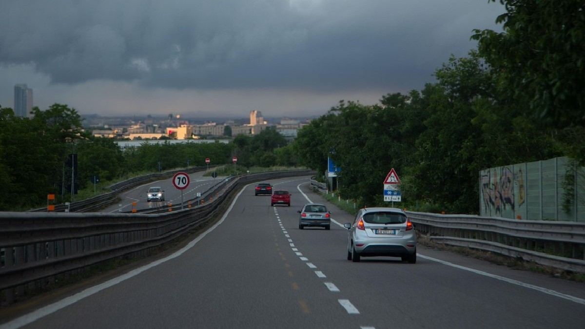 Mai multe mașini circulă pe un drum cu două benzi, cerul este înnorat
