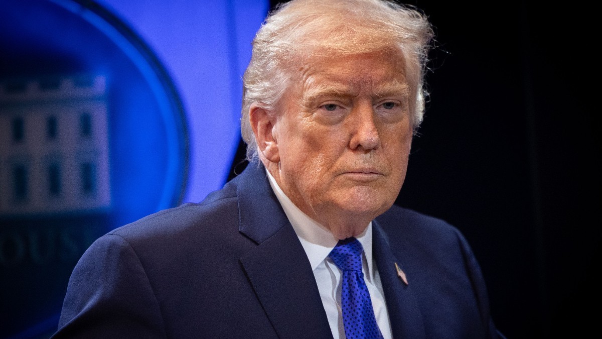 Președintele american Donald Trump îmbrăcat în costum închis la culoare și cravată albastră, privind serios în cadrul unei conferințe oficiale.