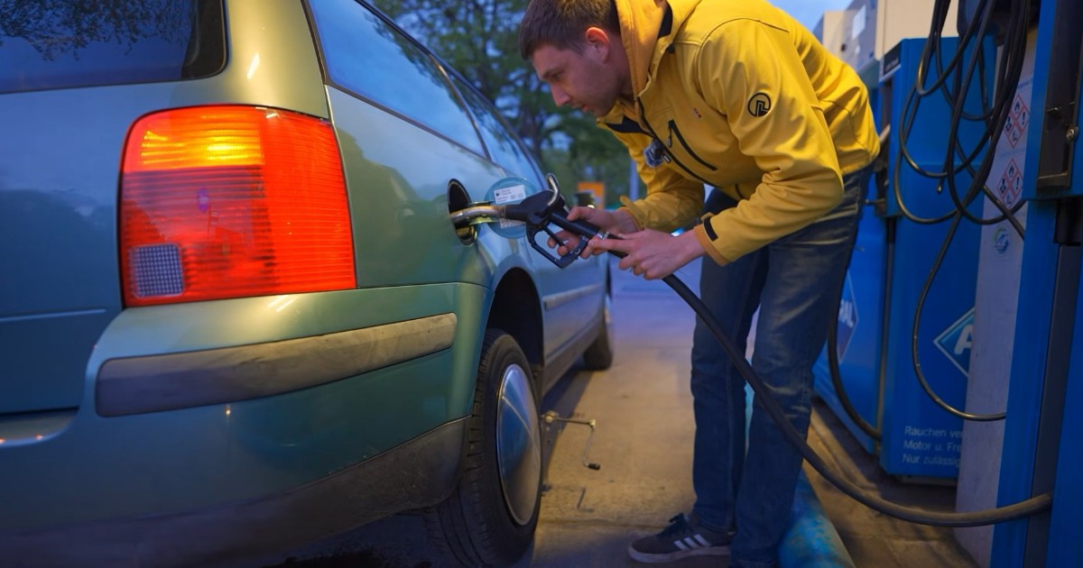 Un tânăr îmbrăcat cu o jachetă galbenă care alimentează cu combustibil un autoturism Volkswagen Passat, la o stație peco.