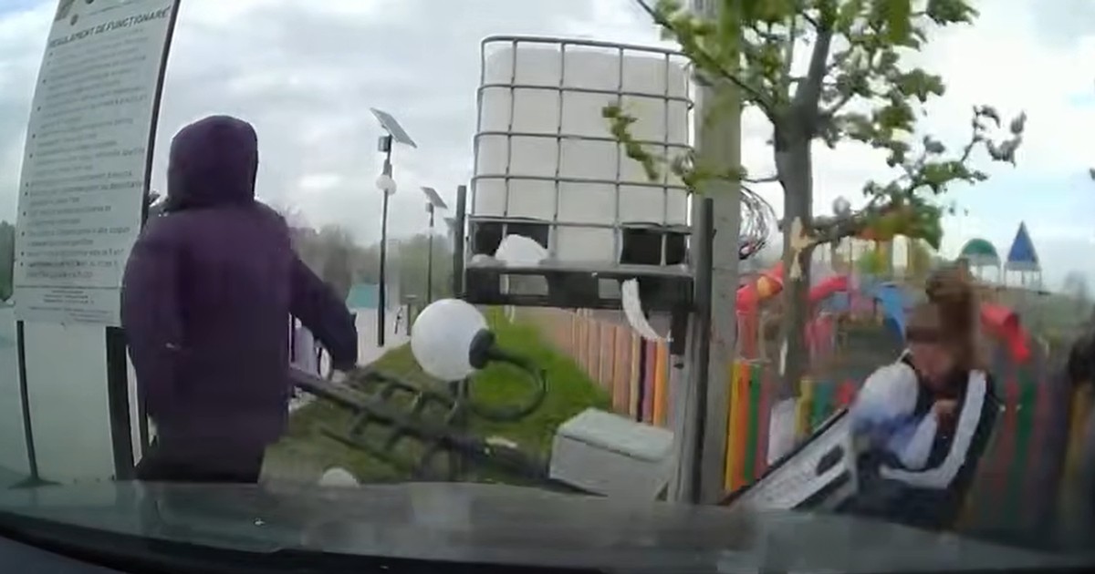 Un bărbat cu glugă pe cap trece pe lângă un stâlp care cade doborât de furtună și lovește o femeie ce ținea în brațe un bebeluș