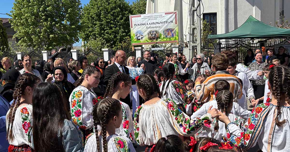 O multime de oameni si copii imbracati in costume populare s-au prins intr-o horă în fata unei biserici