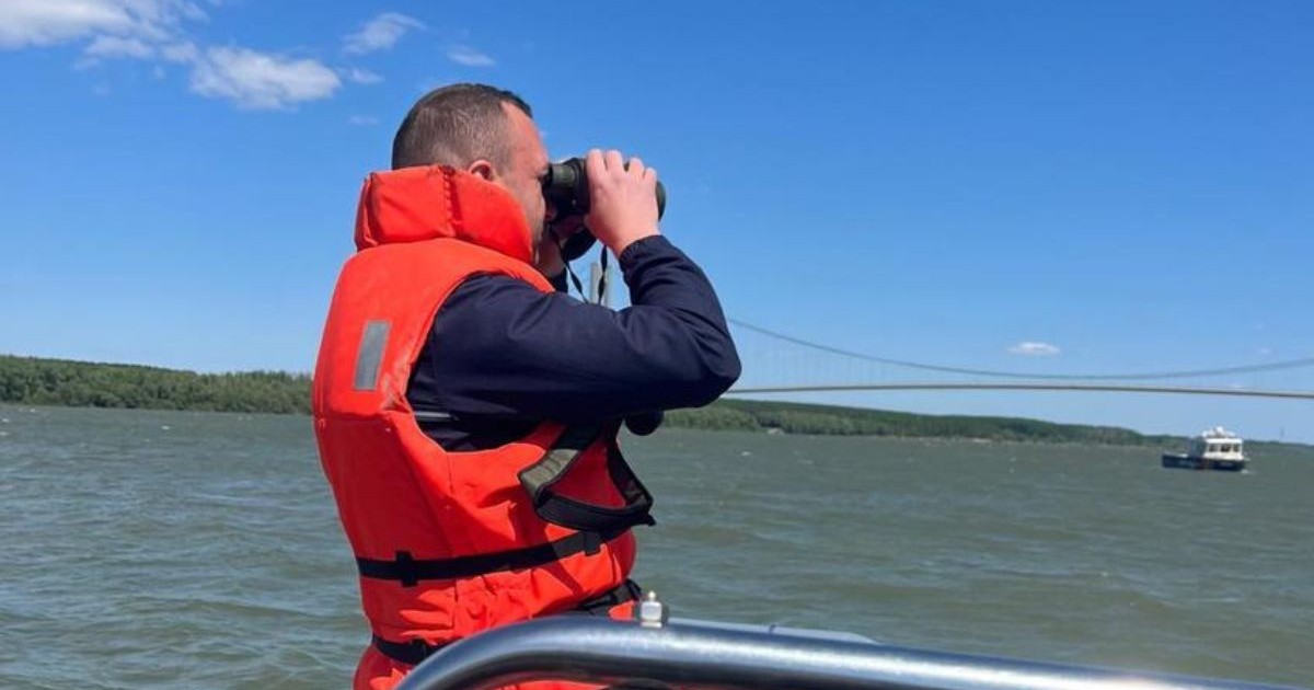 bărbat cu vestă de salvare culoare portocaliu fosforescent, aflat pe o barcă, în timp de privește prin binoclu