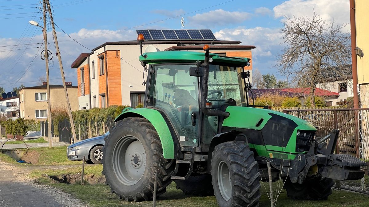Un tractor verde este parcat pe spațiu verde, în fața unei clădiri, într-o zonă cu blocuri mici și case