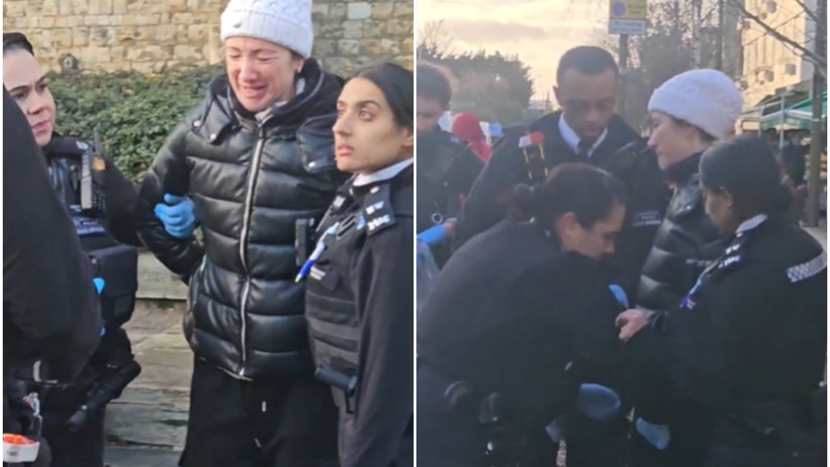 O femeie cu geacă neagră și căciulă albă, pe stradă, în timp ce este reținută de polițiști.