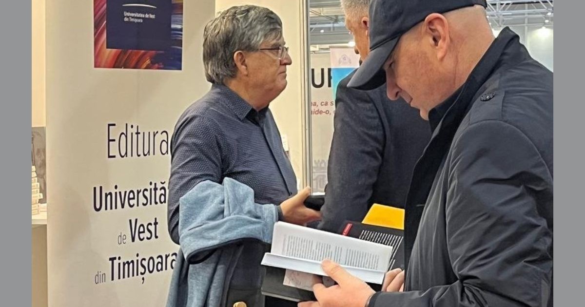 ilie bolojan, cu o șapcă neagră pe cap și îmbrăcat într-p geacă neagră de fâș cu guler, privind în jos, spre o carte deschisă pe care o ține în mâini, la standul Universității de Vest din Timișoara. Târgul de Carte Gaudeamus, 6 decembrie 2025