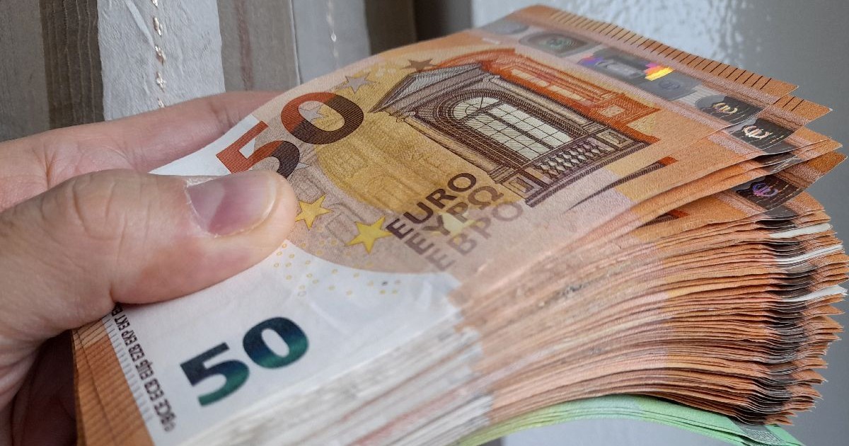 O fotografie în prim-plan a unei mâini care ține un teanc gros de bancnote de 50 de euro..