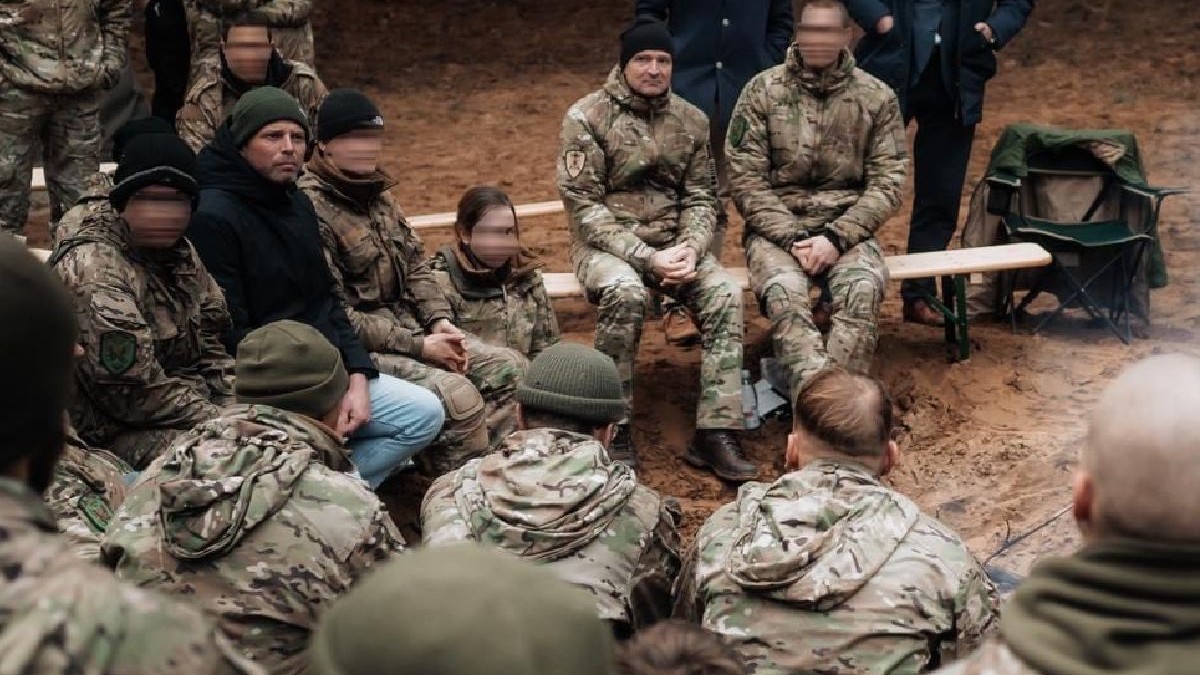 Fotografie dintr-o sesiune de antrenament militar: soldați în uniforme de camuflaj stau pe bănci, în mijlocul uneii păduri.