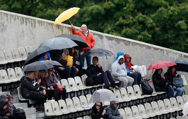 epa05323187 People sitting in the rain as the first round matches are interrupted at the French Open tennis tournament at Roland Garros in Paris, France, 22 May 2016. EPA/ETIENNE LAURENT