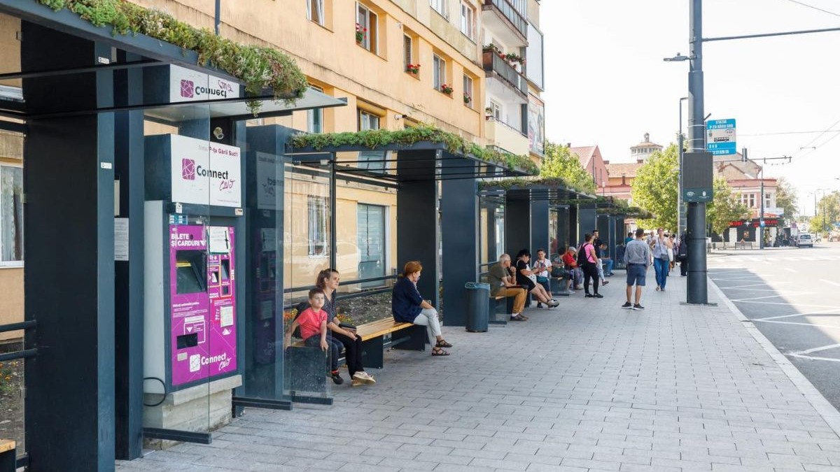 statie de autobuz din cluj, cu oameni care stau pe banci si asteapta autobuzul