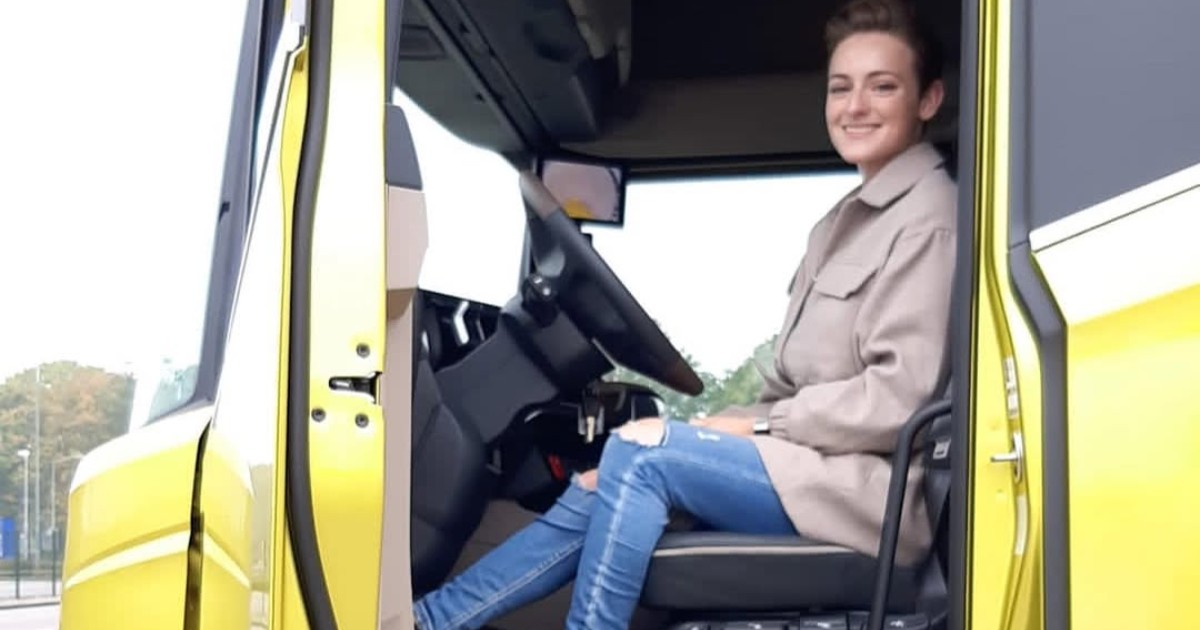O tânără în timp ce stă la volanul camionului ei galben, poartă o pereche de jeanși și un palton