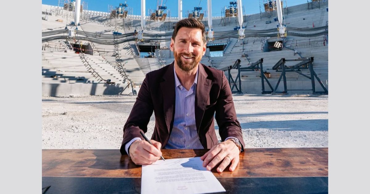 Lionez Messi, îmbrăcat într-o cămașă roz și un sacou macro, stând la un birou de lemn masiv în timp ce semnează un contract, octombrie 2025, Miami