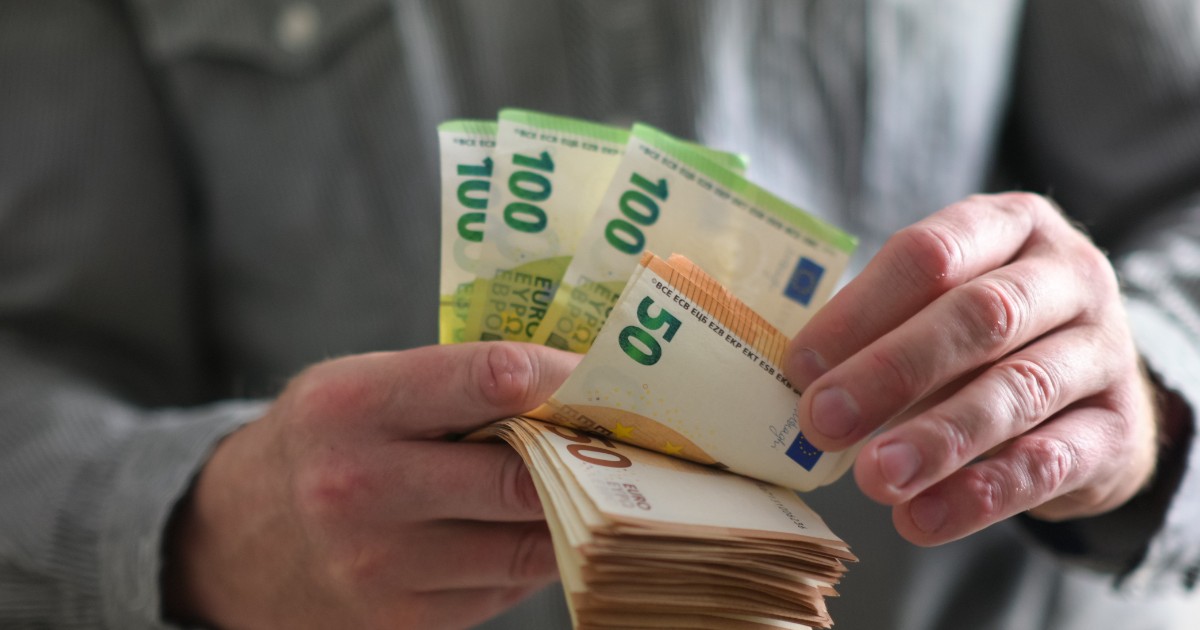 Un bărbat italian îmbrăcat cu o cămșă gri, în timp ce numără un teanc de bani. Hârtiile sunt de câte 50 și 100 de euro.