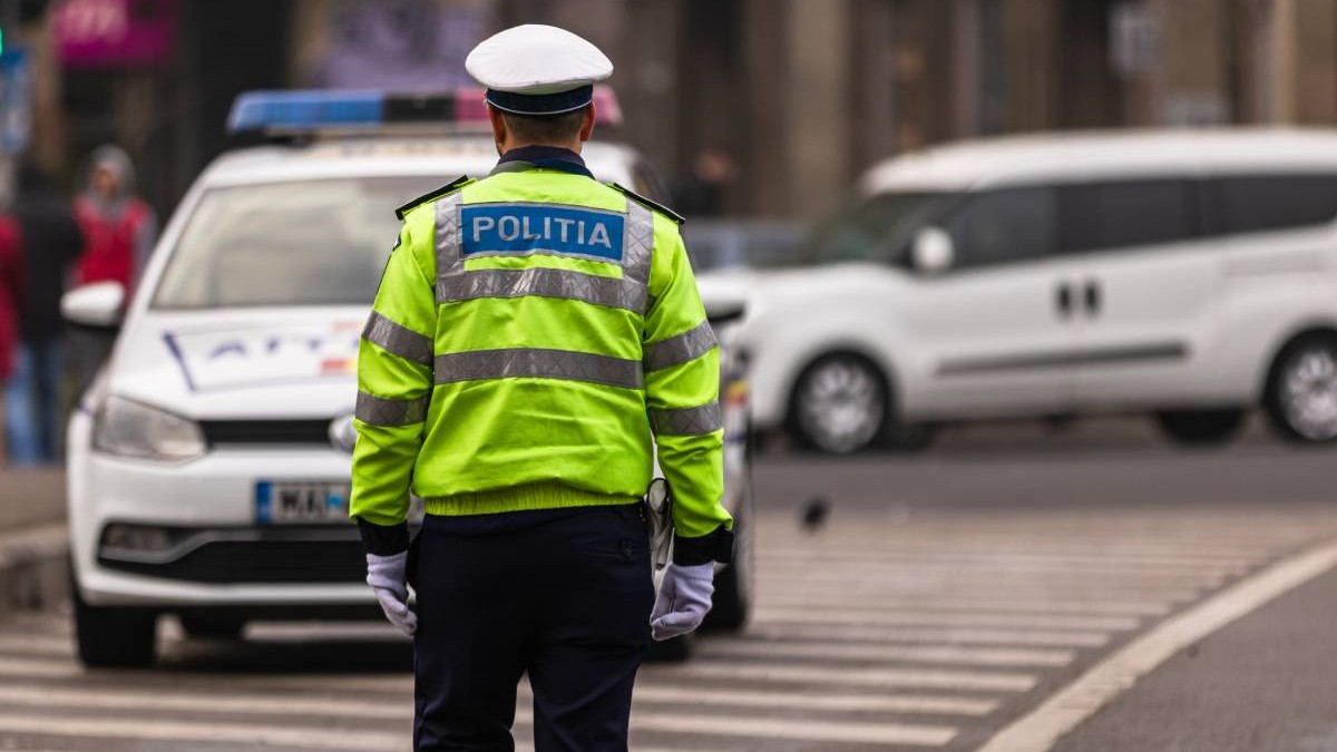 politist imbracat in uniforma in fata lui este autospeciala de politie