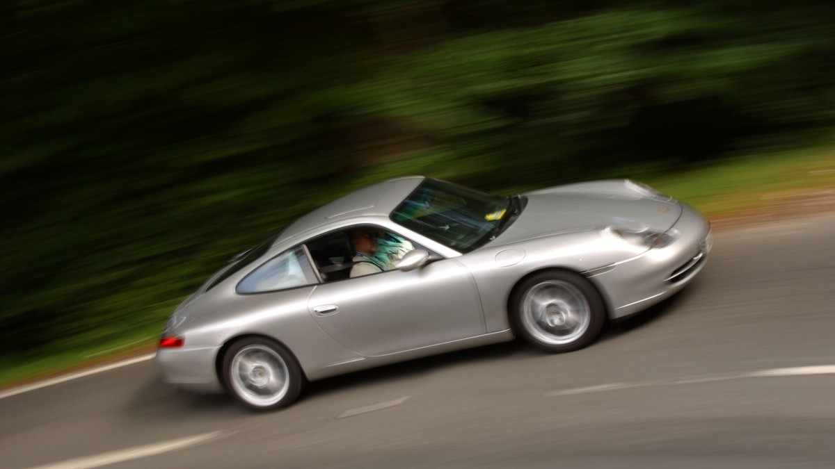 Imagine cu un șofer într-un Porsche gri. Acesta merge cu viteză pe un drum