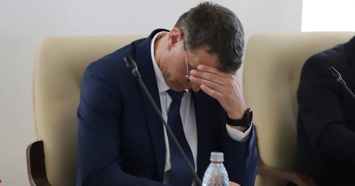 Ionuț Moșteanu, ministrul Apararii si membru USR, in sacou inchis la culoare, camasa amba si cravata neagra, asezat la birou, priving in jos, cu mana stanga peste ochi si frunte