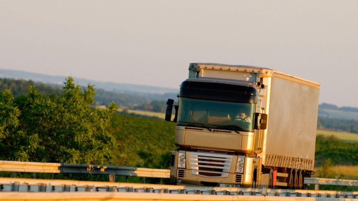 Un camion cu remorca în timp ce se deplaseaza pe un drum in Franța, pe marginea drumului se vad arbusti