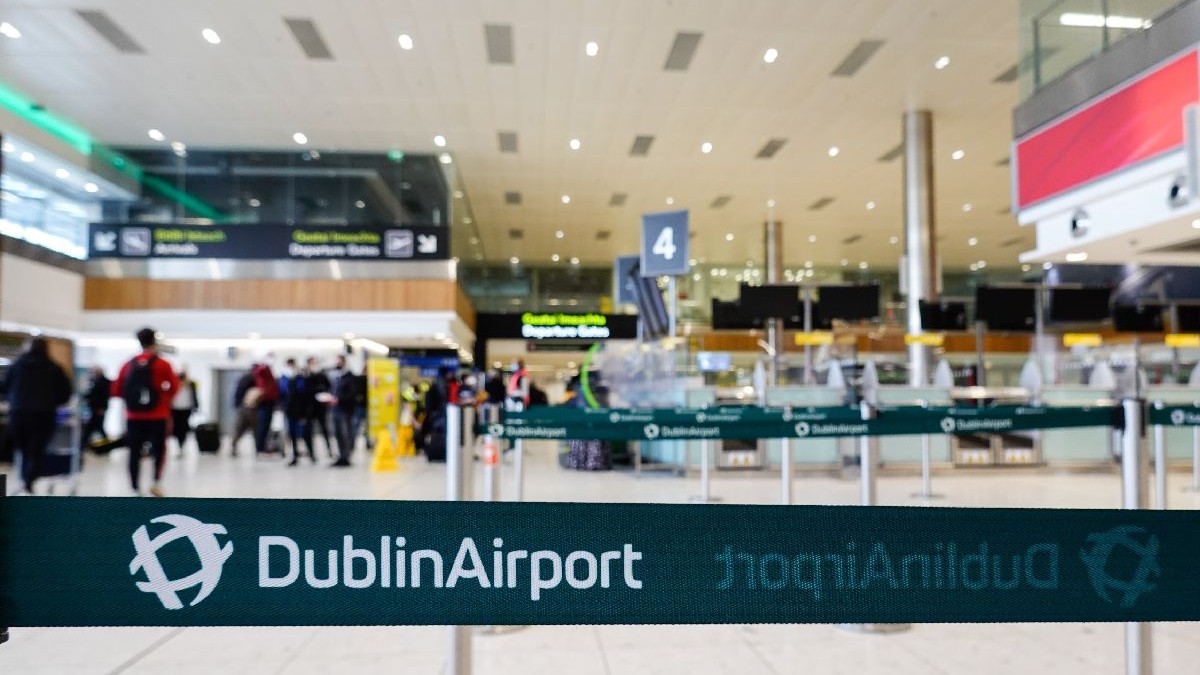 O bandă cu inscripția Dublin Airport, în prim plan, iar în spate mai mulți oameni pe un culoar larg al aeroportului din capitala Irlandei