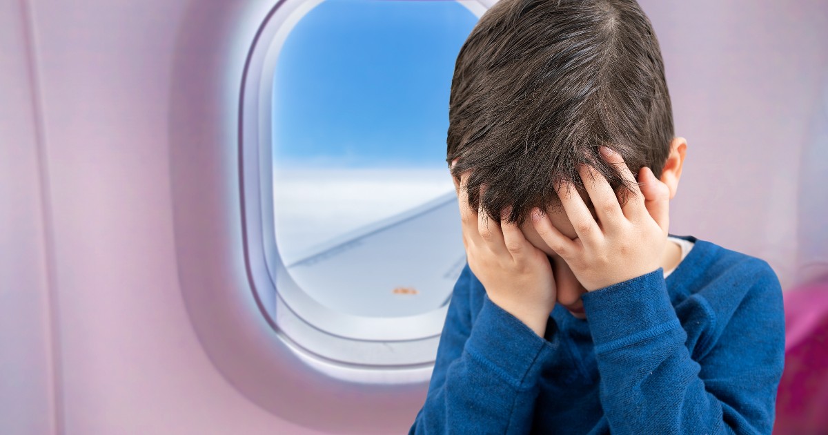 În imagine se vede un copil așezat într-un avion, lângă hublou, cu mâinile pe față și capul plecat. Expresia și postura sa sugerează că este supărat, copleșit sau stresat în timpul zborului.