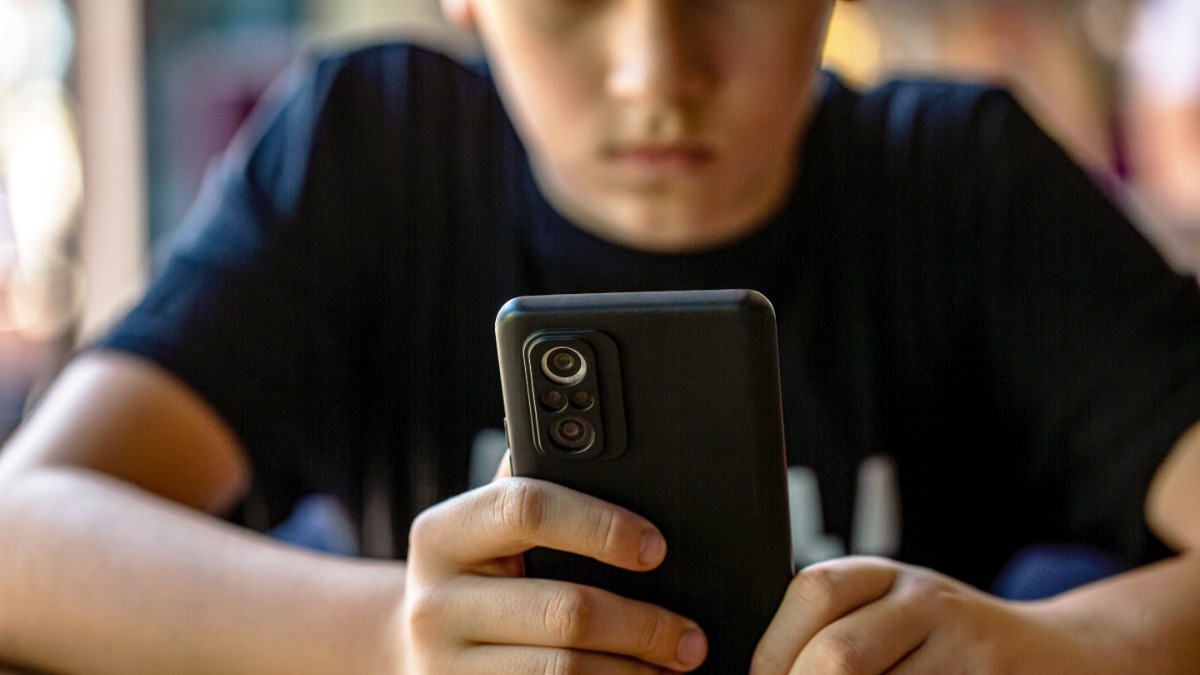 Un băiat îmbrăcat în negru care ține un telefon în mână