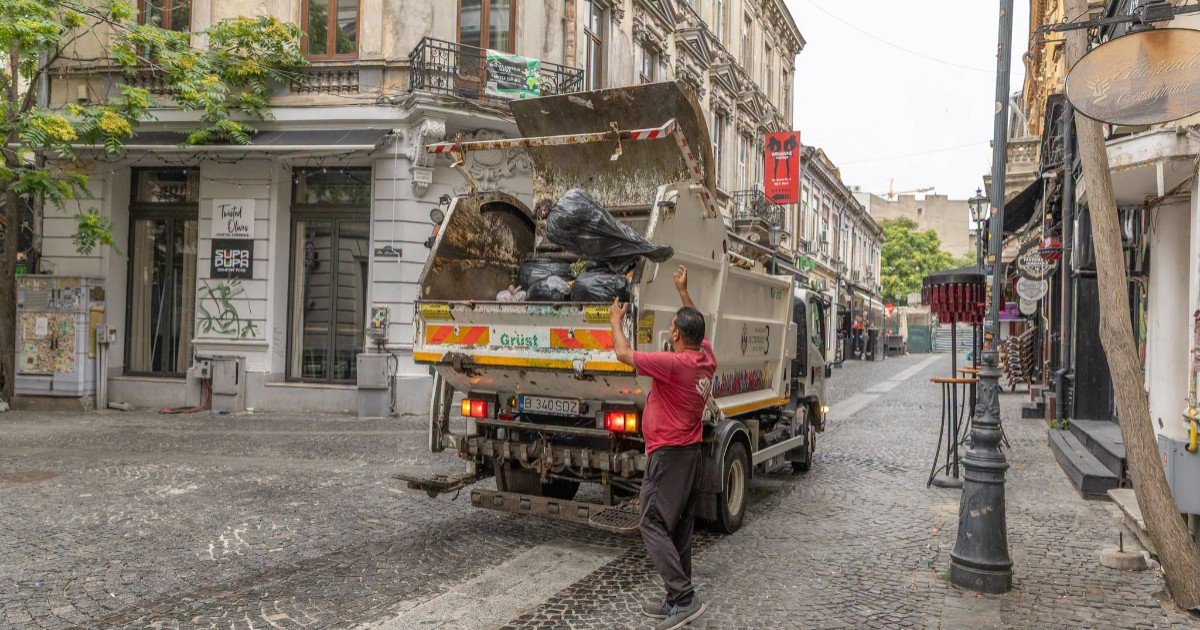 O mașină de gunoi în centrul Bucureștiului, un bărbat adună sacii cu deșeuri și îi aruncă în camion