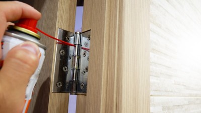 De ce scârțâie ușa și cum o repari - Un bărbat unge balamalele de la o ușă cu un spray special