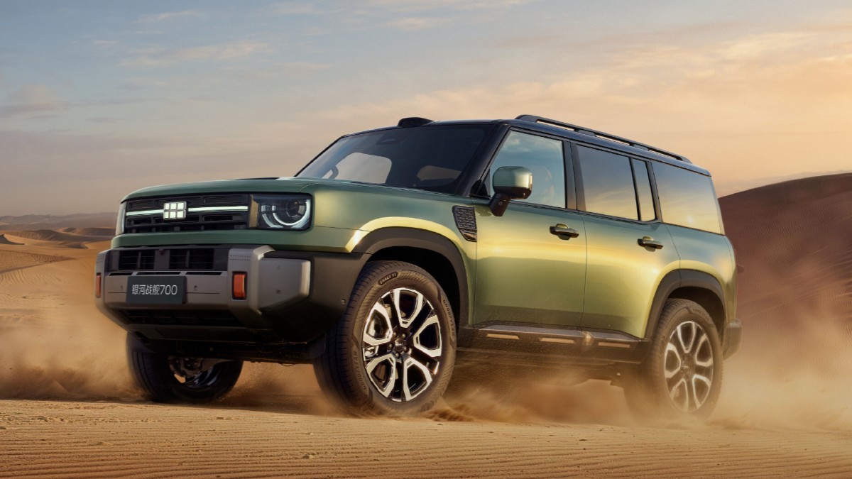 Un SUV off-road, de culoare verde măsliniu, rulând prin dunele de nisip ale unui deșert la apus.